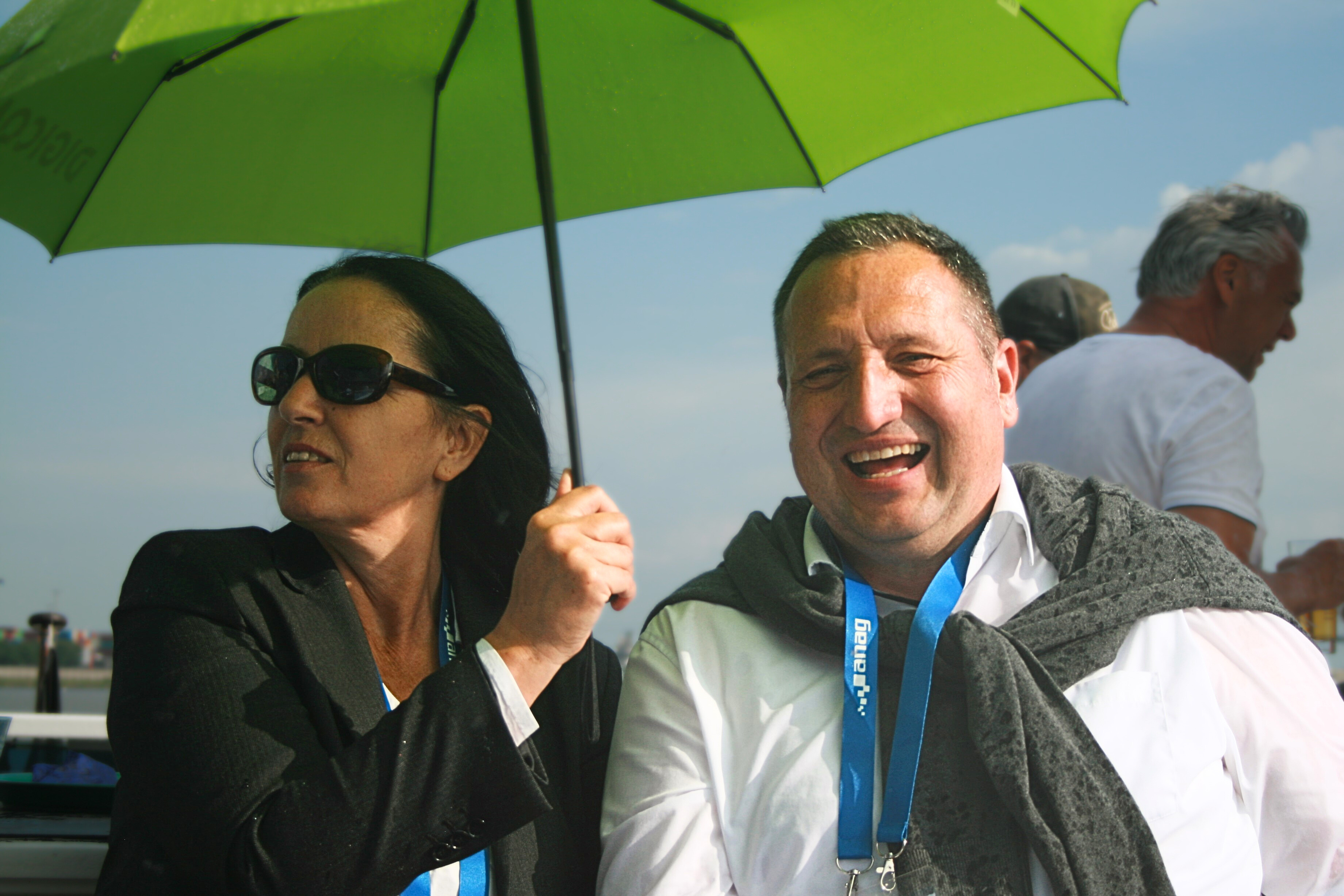 Eine ANAG Mitarbeiterin und ein ANAG Mitarbeiter sitzen föhlich und lachend unter einem Regenschirm bei einem Ausflug